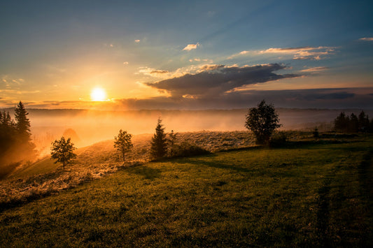 Sun over hills with trees and clouds